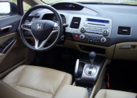 Dashboard and steering wheel of a car with beige leather seats and an automatic gear shifter