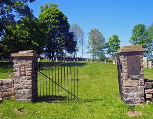 Stone gate pillars with a wrought iron gate and bronze plaque, opening onto a grassy path